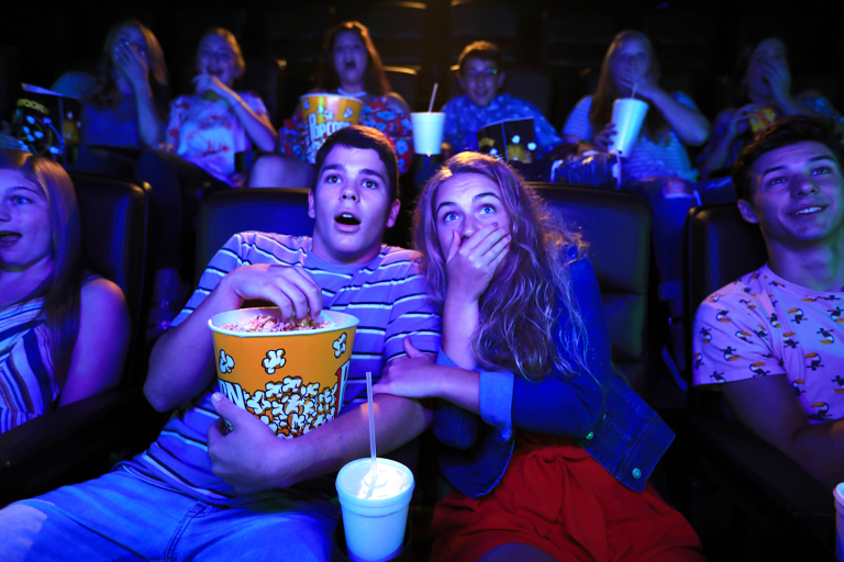 Teens sharing popcorn and watching a movie in the theater