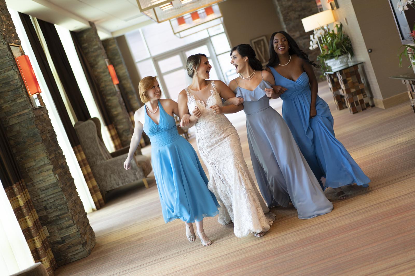 A bride and three bridesmaids strolling down a hallway with their arms linked