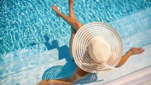 Woman relaxing on pool stairs with a large sunhat on