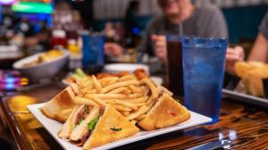 Close up of a club sandwich with fries and a man smiling in the background