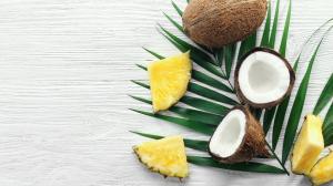 An assortment of cut coconuts and pineapple slices on a green palm leaf on a wooden surface