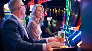 A middle-aged couple smiling as they play slot machines in a vibrant, colorful casino setting.
